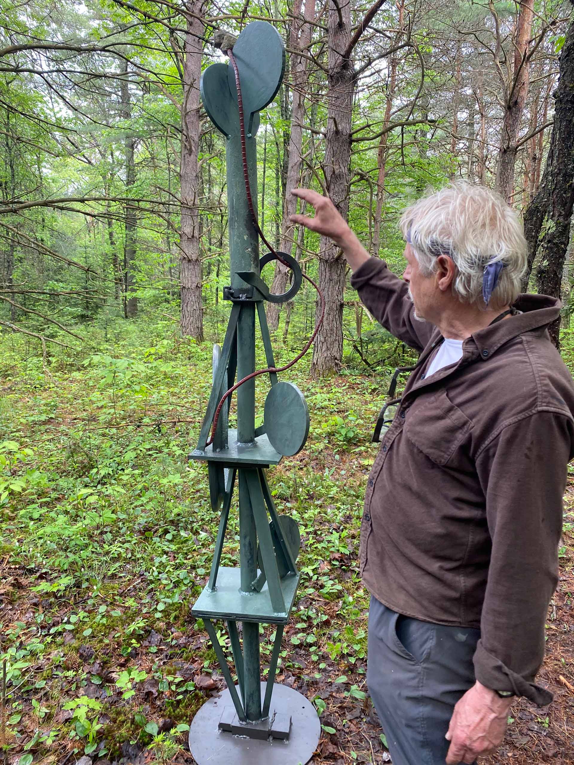 Barney Bellinger gesturing towards his artwork in the woods