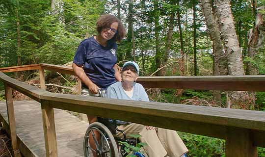 Young woman pushing senior citizen in wheelchair along trail