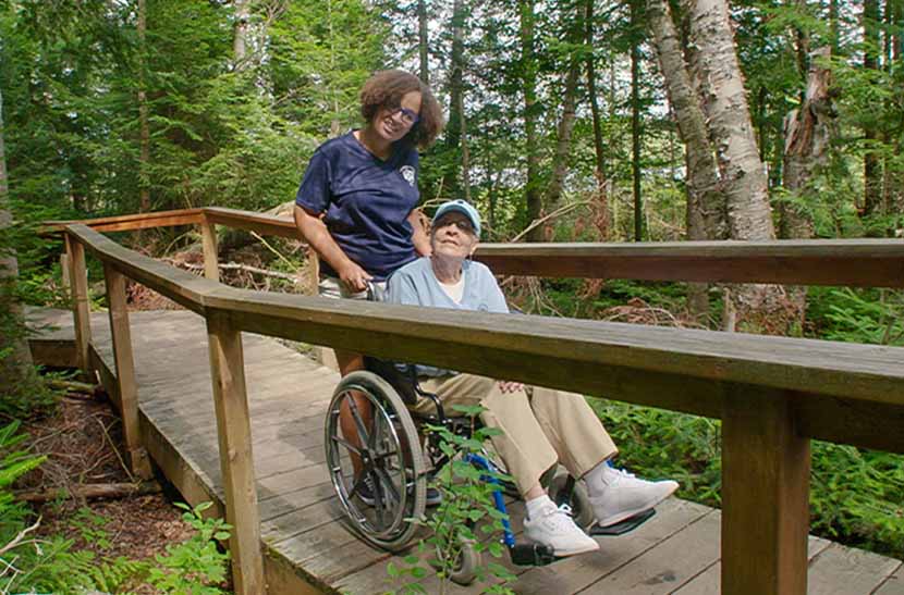 Young woman pushing senior citizen in wheelchair along trail