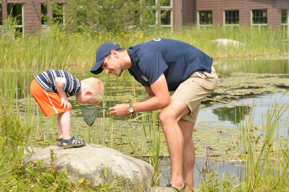 Wild Center guide showing child contents of fishing net, near side of pond.