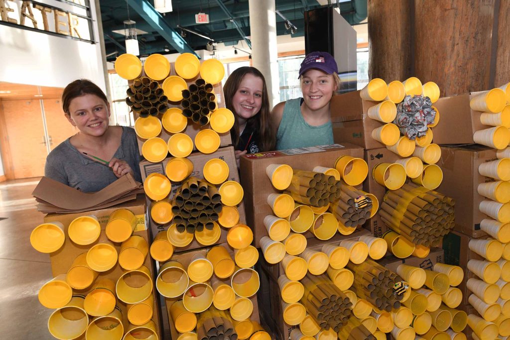 Three students posing with beehive exhibit