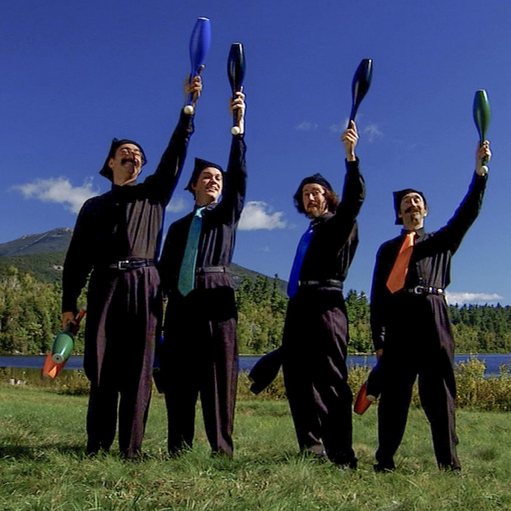Four jugglers outdoors raising their clubs in unison