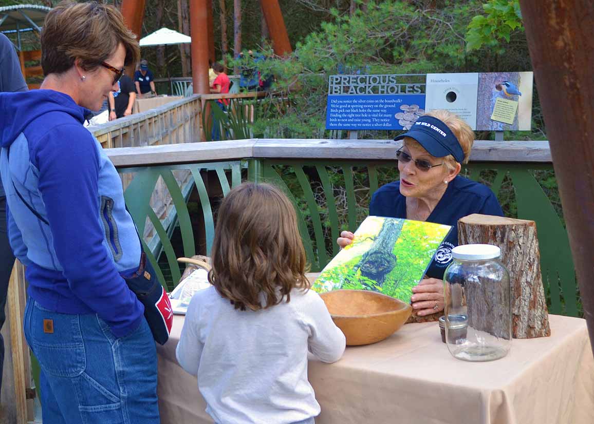 Woman at table outdoors explaining exhibit to guests