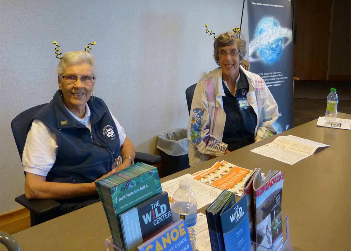 Women at Wild Center desk wearing bug-style antenna headpieces.