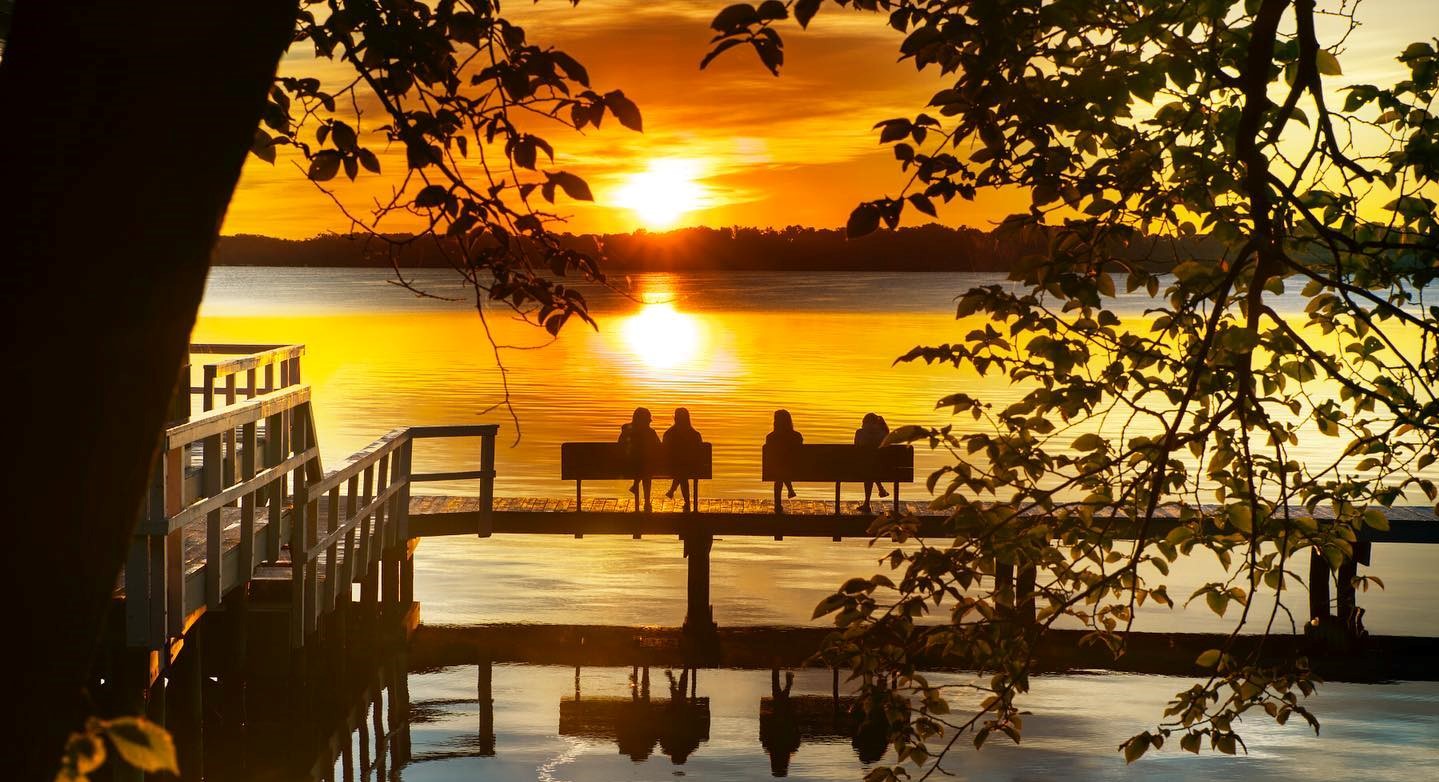 Silhouetted people on pier benches observing sunset on Seneca Lake