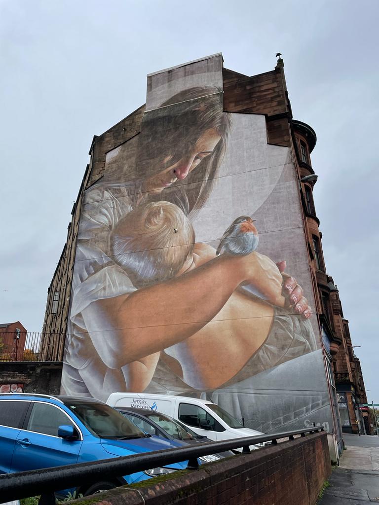 Mural of mother and child on side of building with small bird on hand