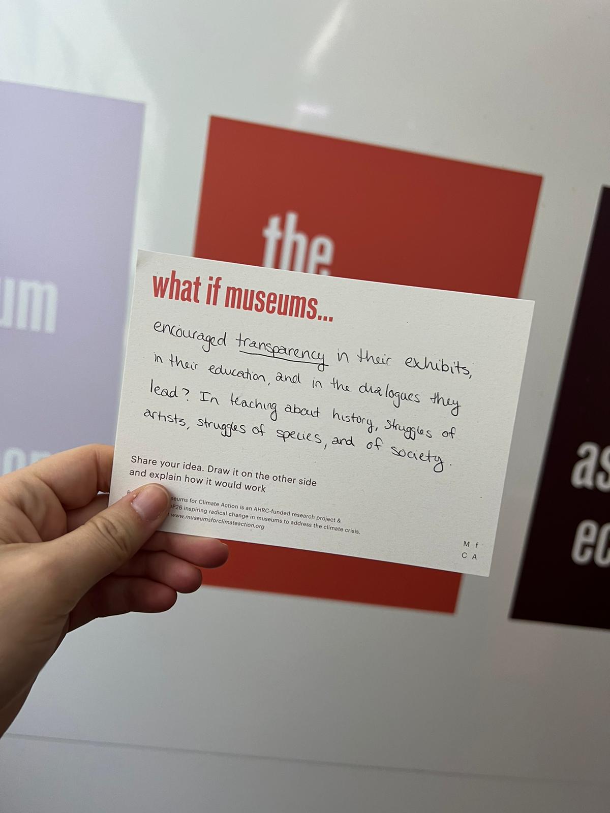 Hand holding postcard with message finishing out "what if museums..." prompt
